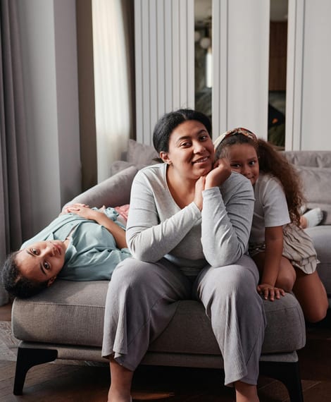 A parent resting on the sofa with two children