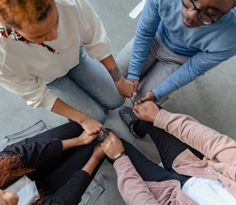 A support group sitting in a circle, hands joined